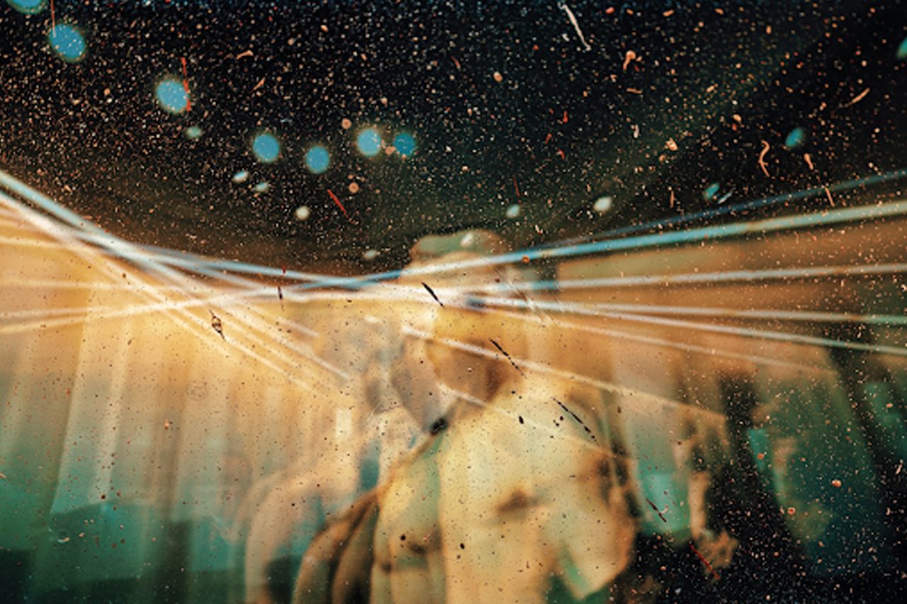 Abstract light rays and dust create a dreamy atmosphere, with a blurred figure faintly visible in the background.