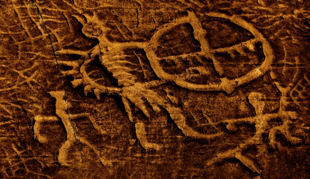 Ancient petroglyphs depicting human figures and a circular symbol on a textured rock surface.