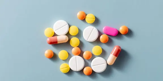 Assorted pills and capsules in various colors scattered on a light blue background.