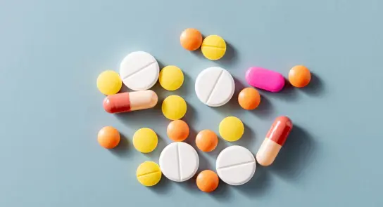 Assorted pills and capsules in various colors scattered on a light blue background.