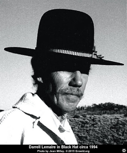 Black-and-white portrait of a man with a mustache wearing a wide-brimmed black hat, set against a rugged landscape.