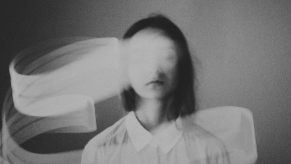 A blurred figure with a white shirt, surrounded by flowing, ethereal ribbons, creating a dreamlike atmosphere.