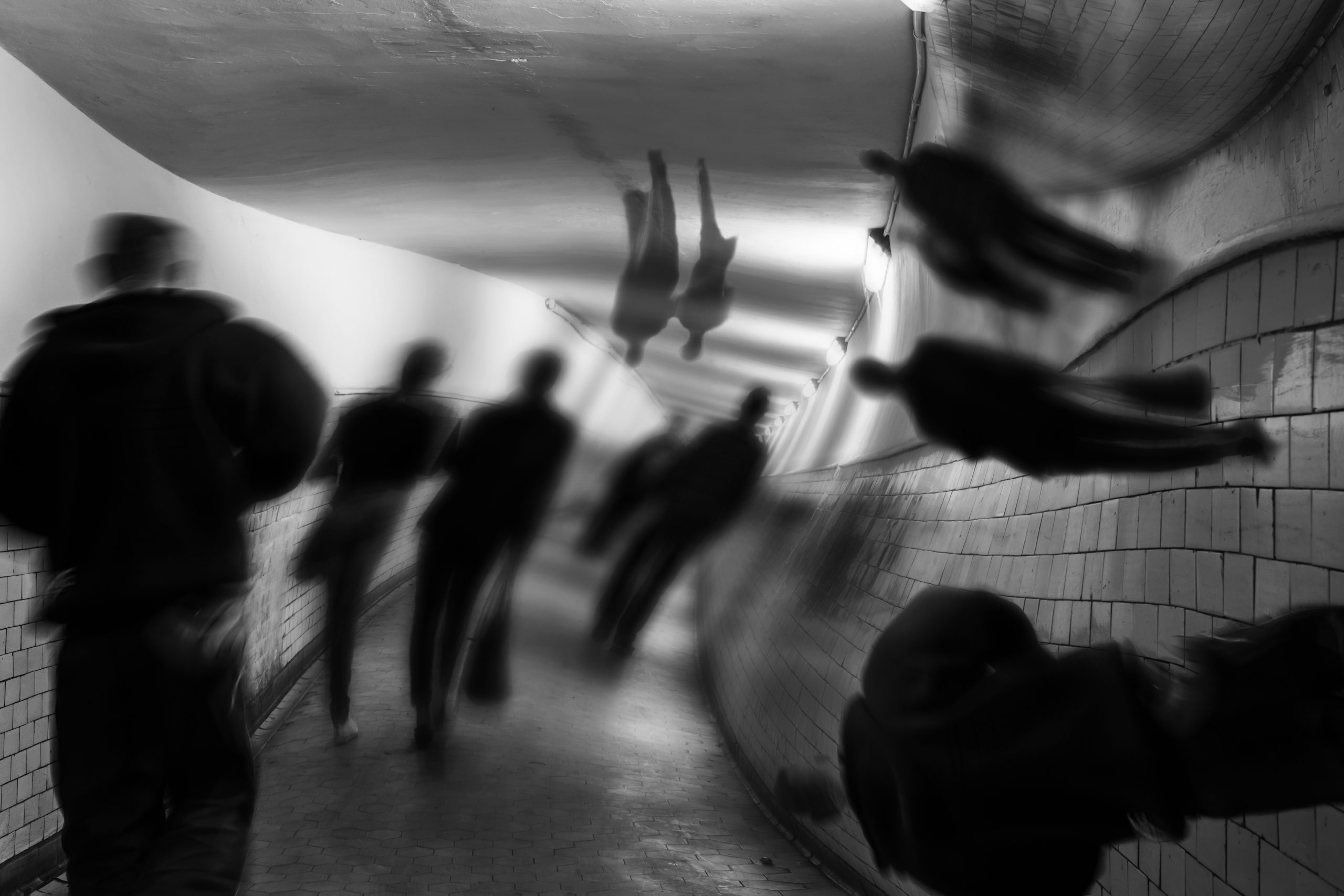 Blurred figures walking through a dimly lit tunnel, with distorted reflections on the curved walls.