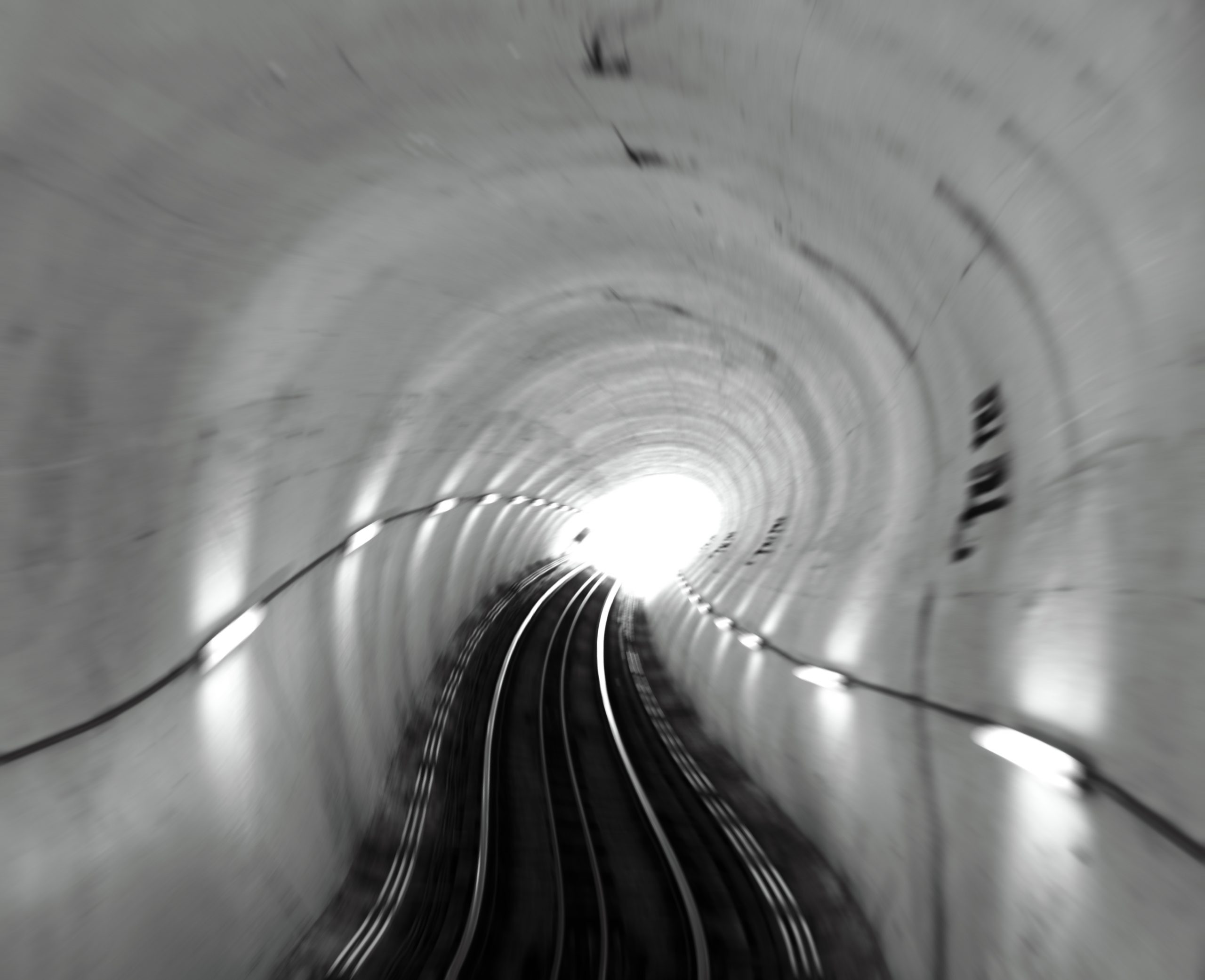 Blurred view of a tunnel with visible tracks leading towards a bright light at the end.