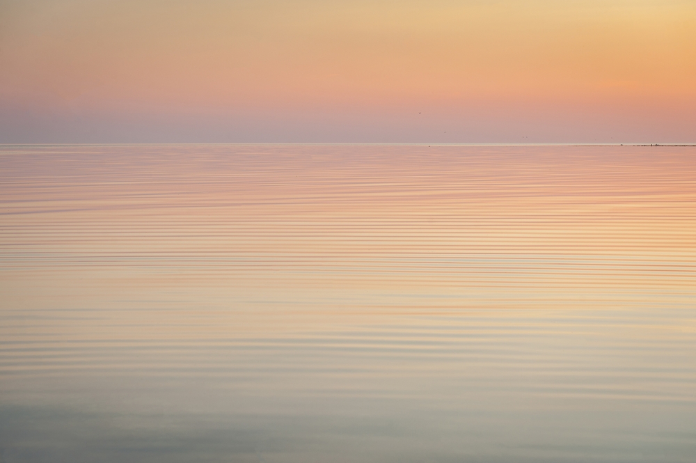 Calm water reflecting soft pastel hues of a sunset, with gentle ripples across the surface.