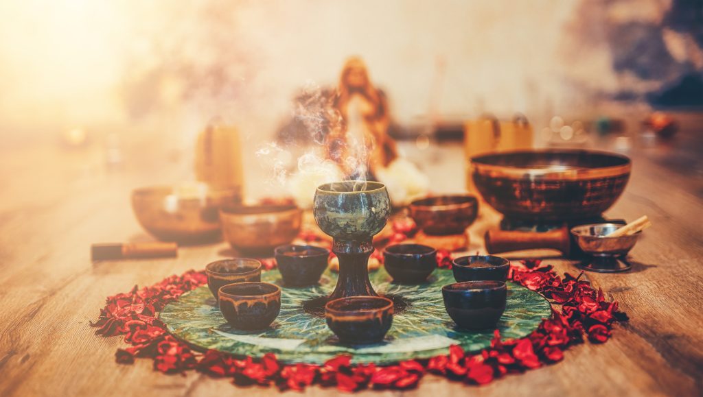 Ceremonial setup with incense burning, surrounded by small bowls and rose petals on a vibrant green mat.