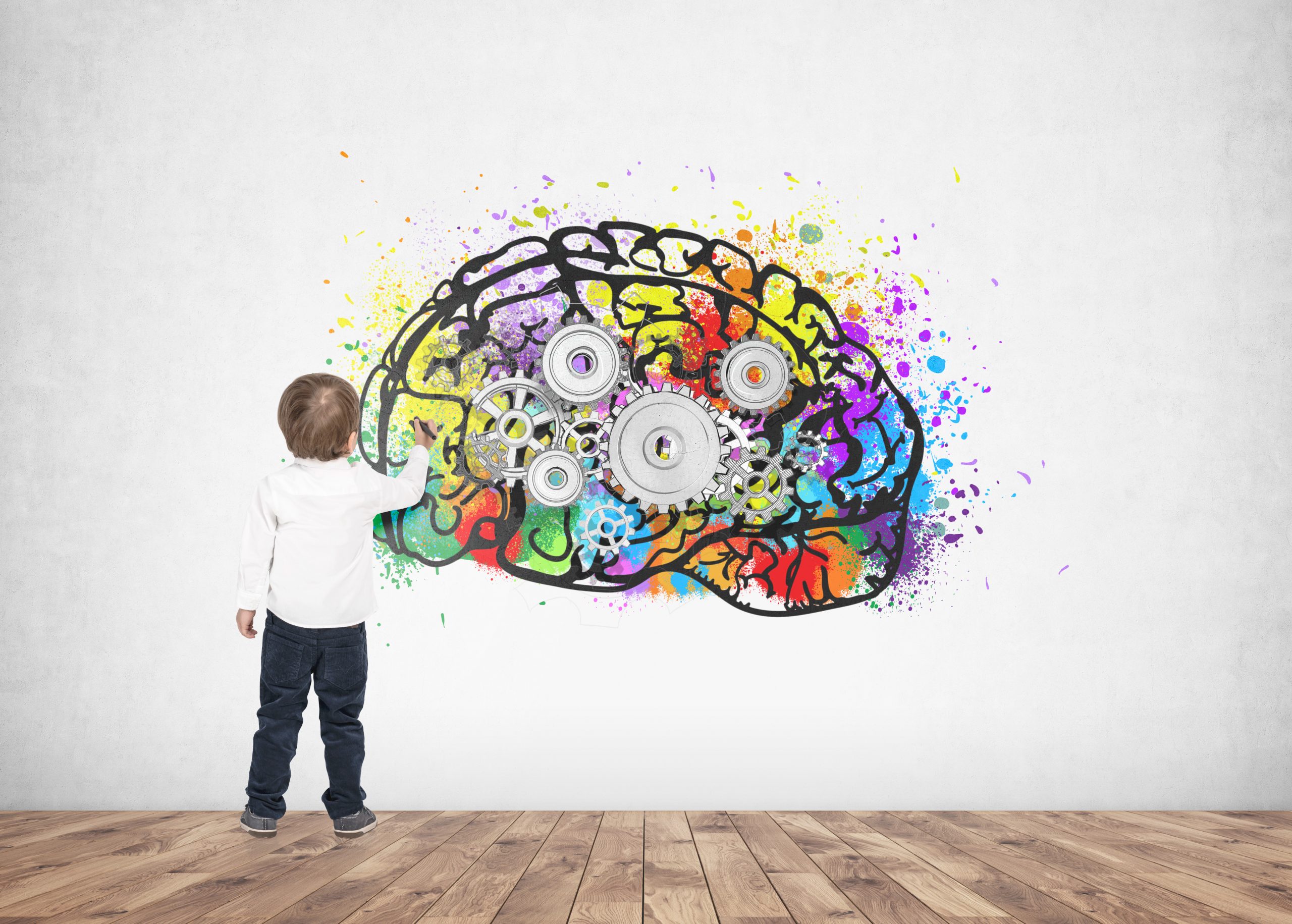 A child interacts with a colorful, gear-filled brain mural on a white wall, set against a wooden floor.