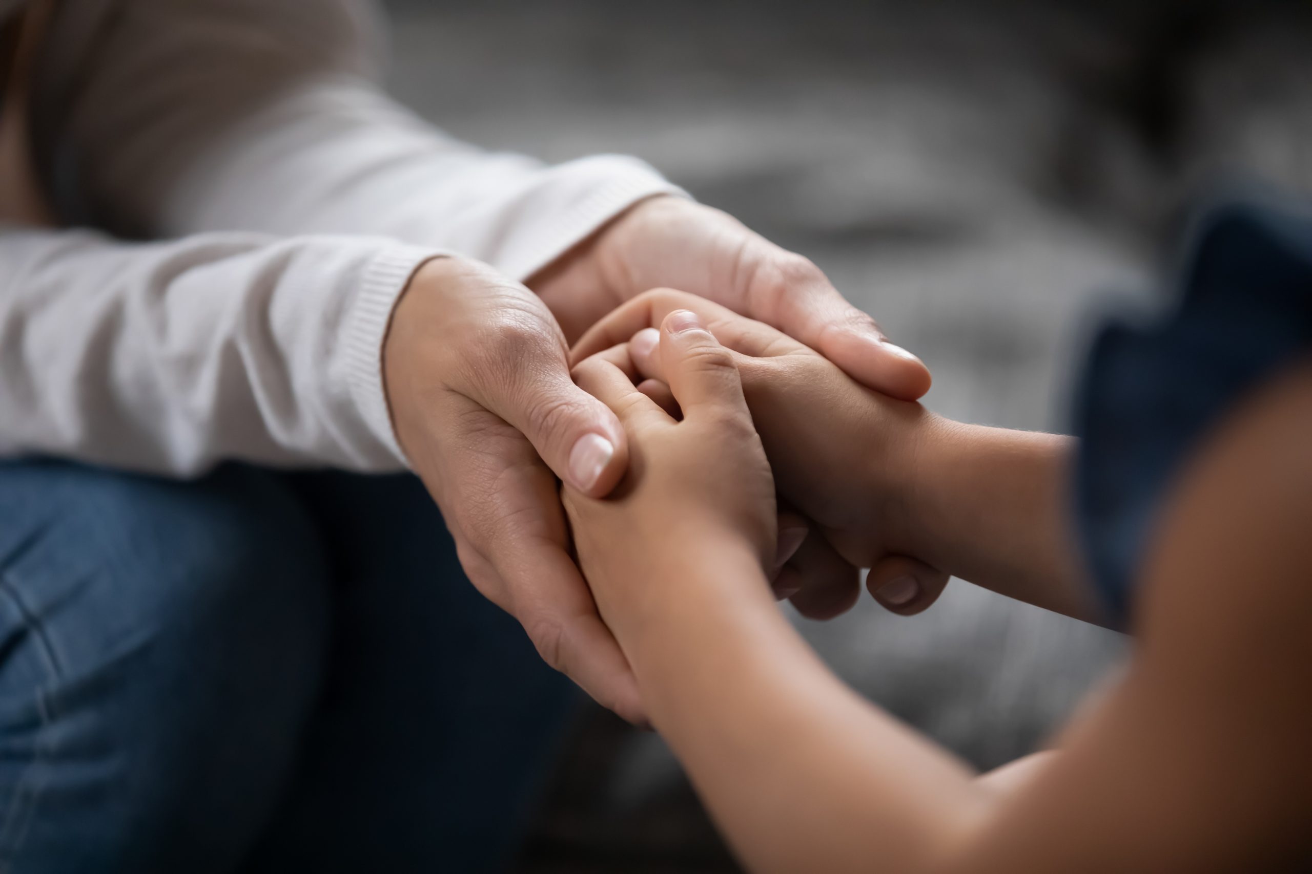 A child's hands clasped in an adult's hands, symbolizing connection and support, with a soft, blurred background.
