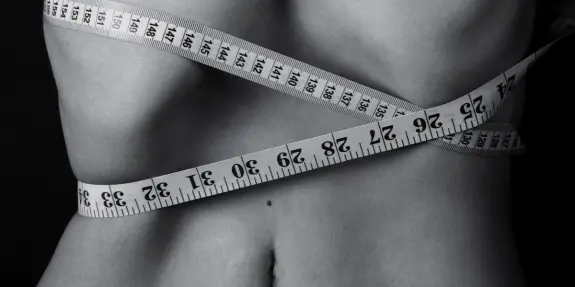 A close-up of a bare torso wrapped with a measuring tape, highlighting the waist and body contours in black and white.
