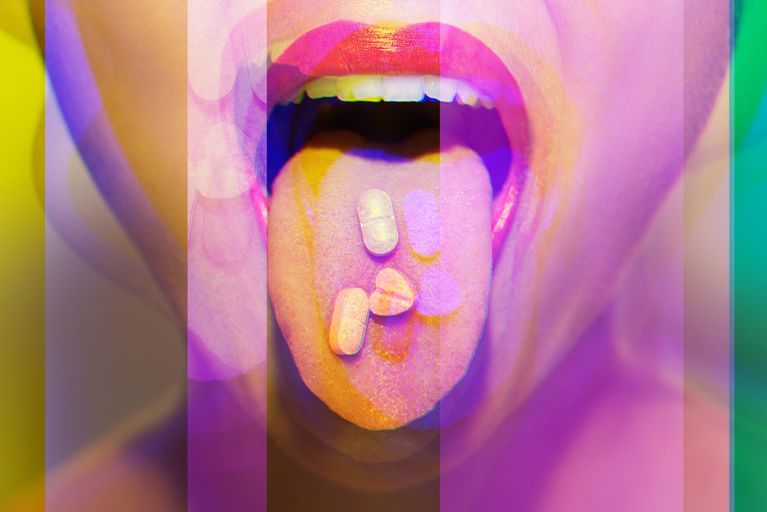 A close-up of a mouth with an open tongue, displaying colorful pills resting on it against a vibrant, blurred background.