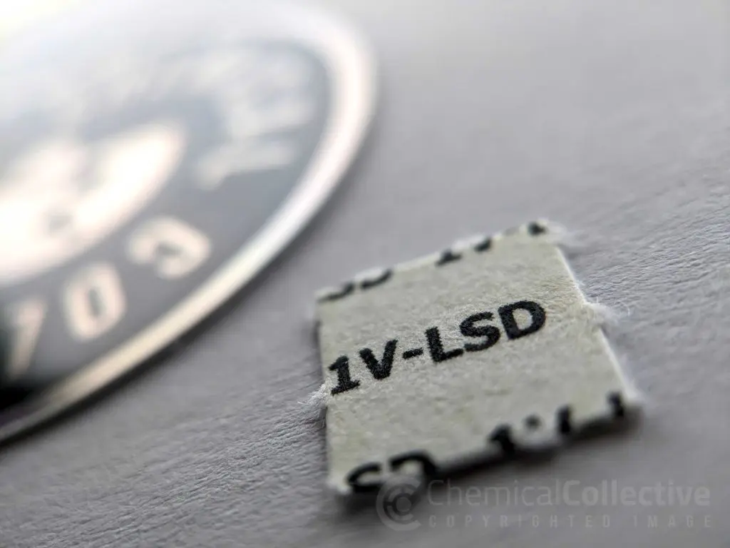 Close-up of a small square blotter paper labeled "1V-LSD" next to a circular design, highlighting intricate details.