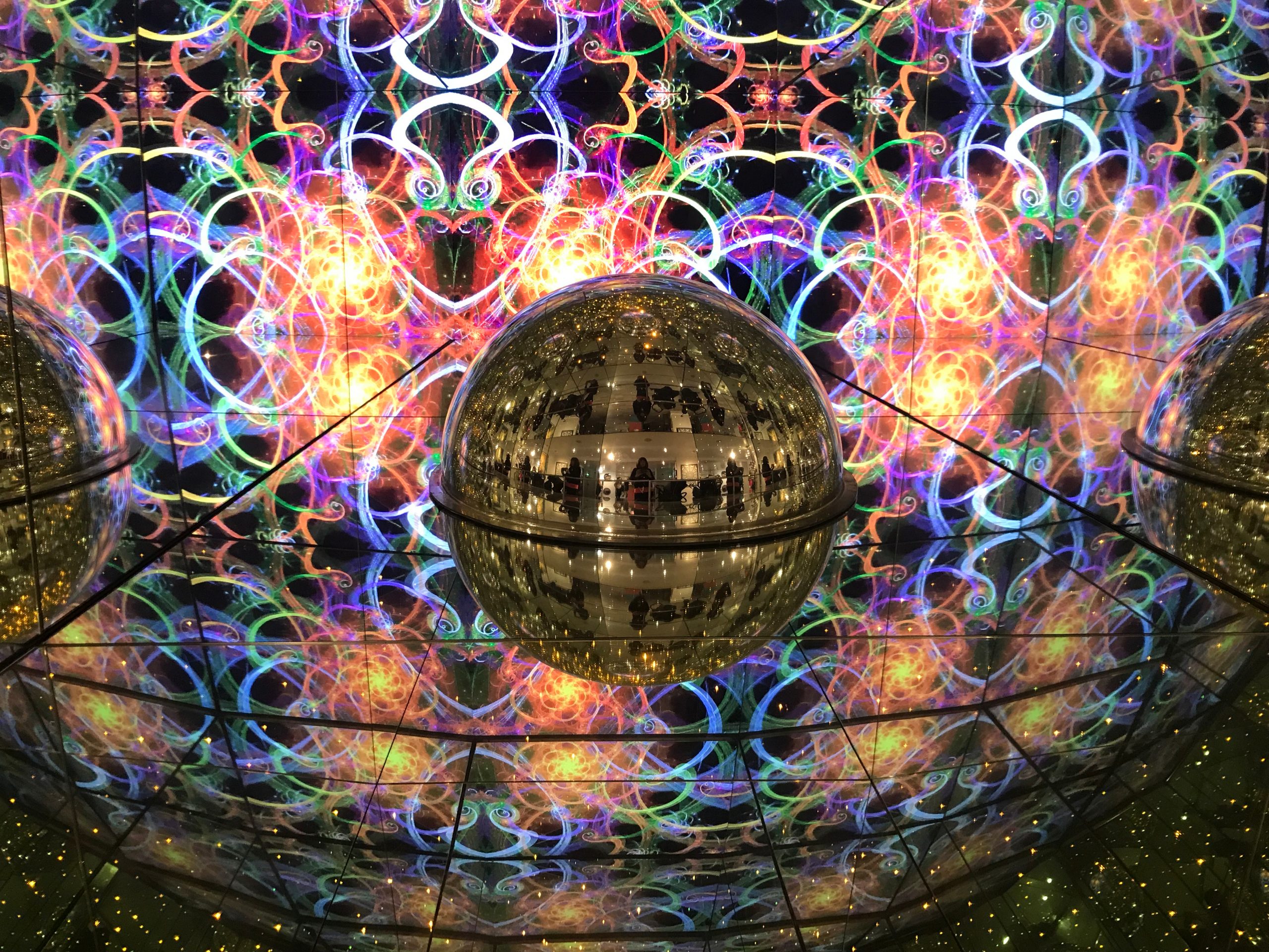 Colorful abstract patterns with swirling shapes and reflections in a mirrored sphere, creating a vibrant, kaleidoscopic ef...