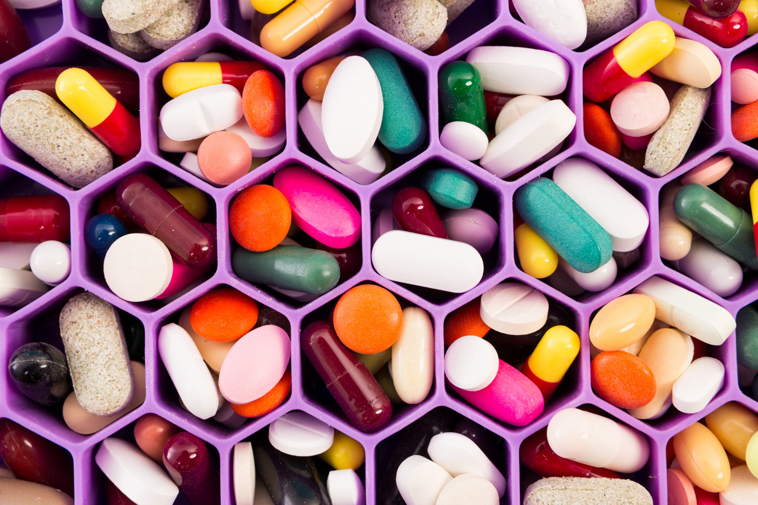 Colorful assortment of pills and capsules arranged in hexagonal compartments.