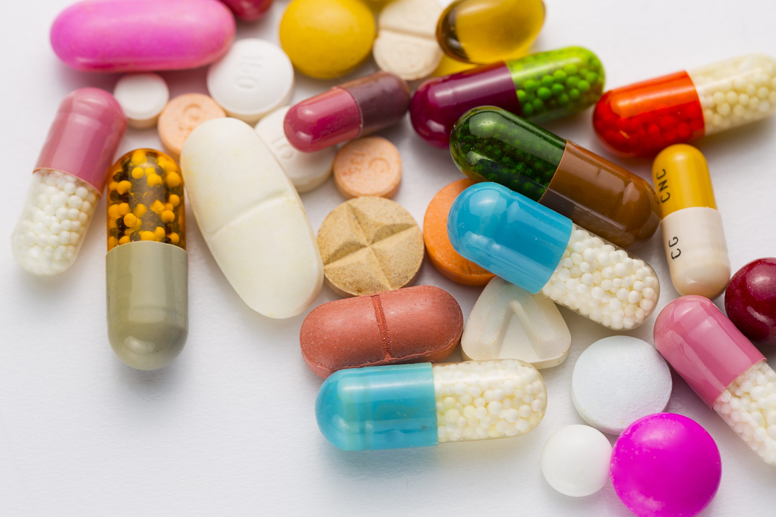 Colorful assortment of various pills and capsules in different shapes and sizes scattered on a white surface.