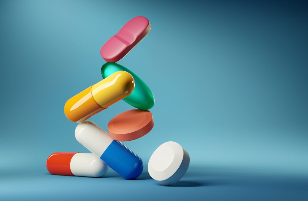 Colorful capsules and tablets stacked and suspended against a soft blue background.