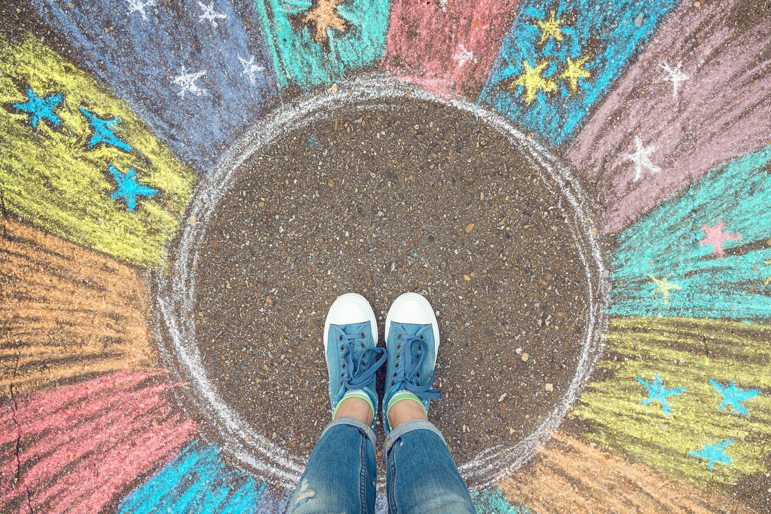 Colorful chalk drawings radiate from a circular center, with a person wearing blue sneakers standing on the edge.