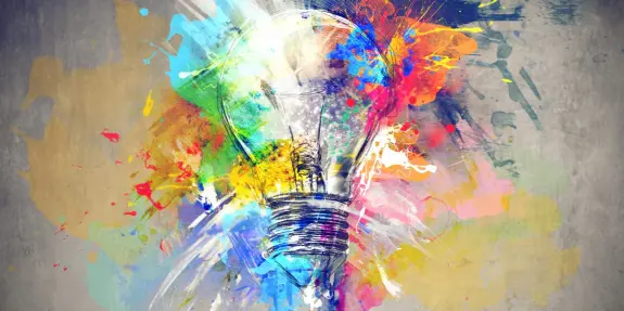 A colorful explosion of paint surrounds a glowing light bulb, symbolizing creativity and inspiration.