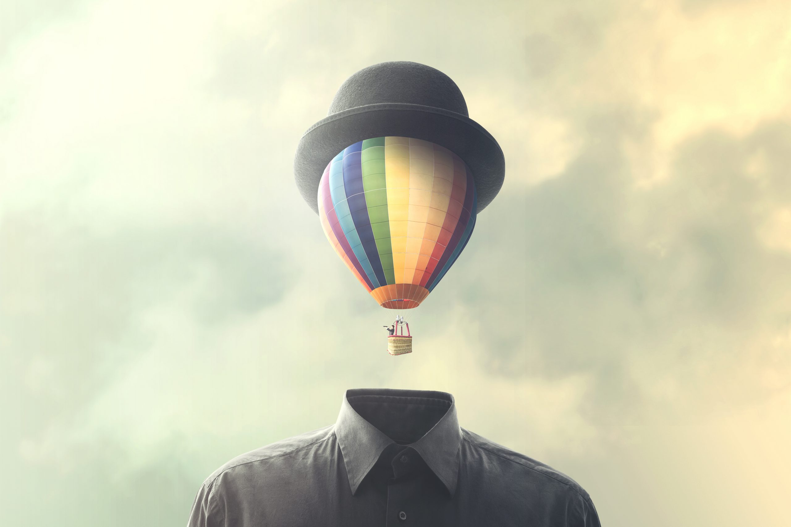 A colorful hot air balloon wearing a bowler hat floats above a headless figure in a gray shirt against a cloudy sky.