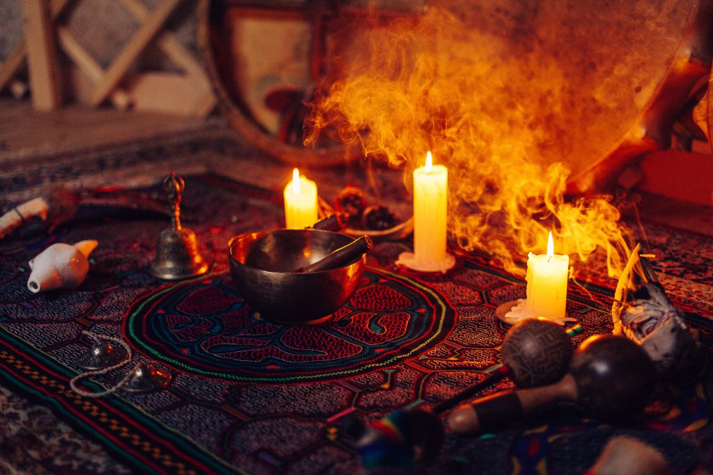 A colorful rug adorned with candles, a singing bowl, and various instruments, surrounded by soft, swirling smoke.