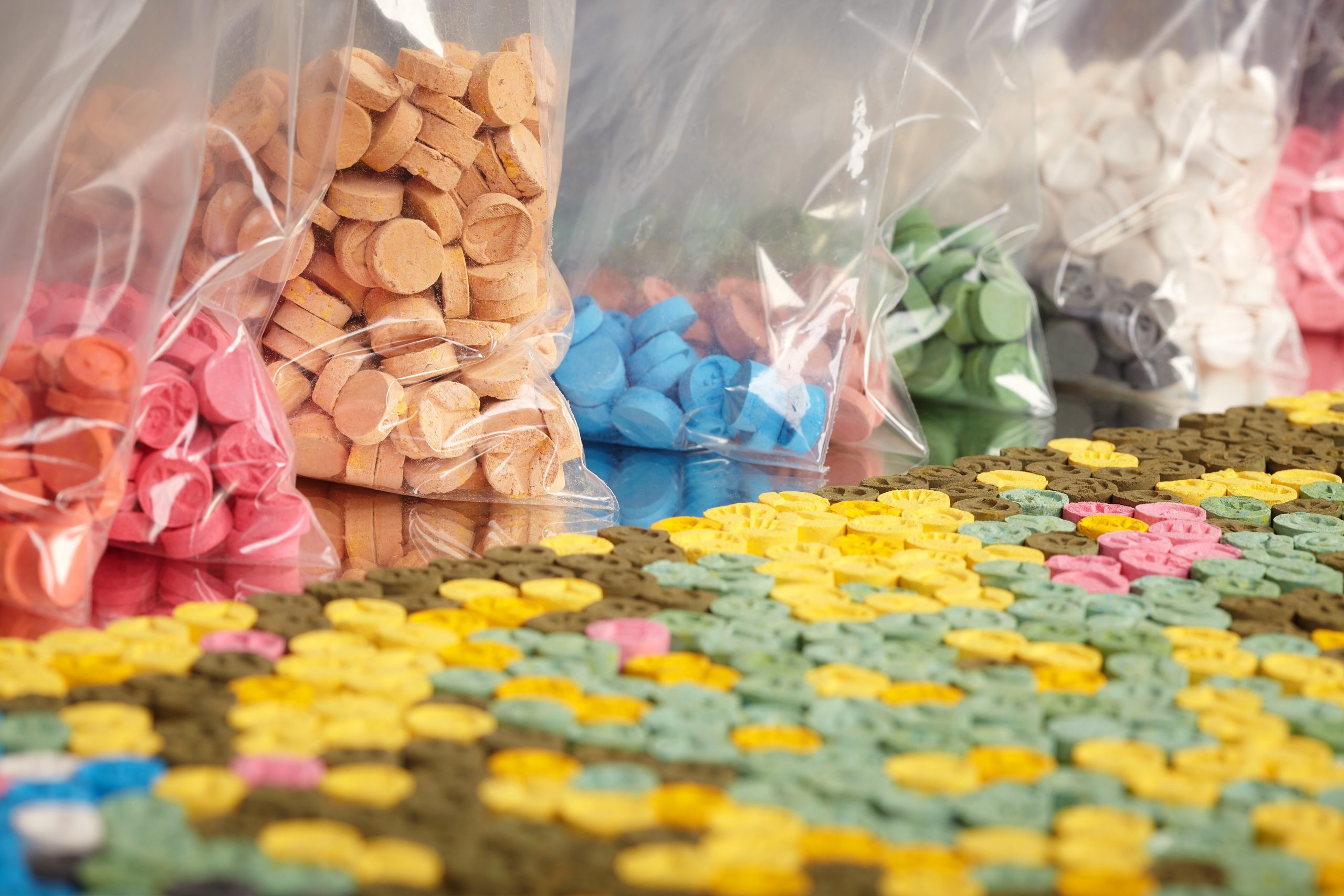 Colorful tablets in various shapes and sizes, neatly arranged with bags of similar candies in the background.