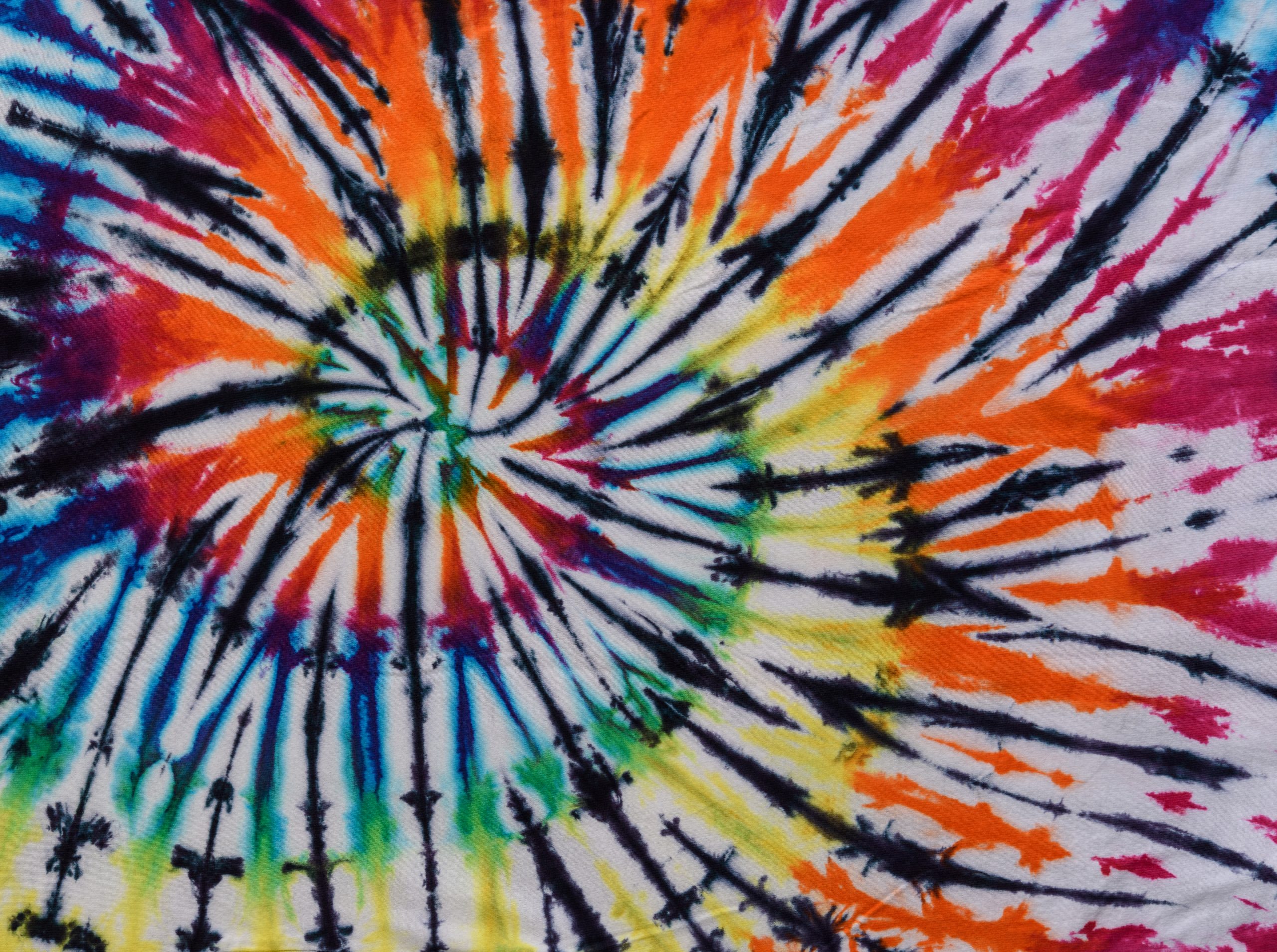 Colorful tie-dye pattern featuring vibrant swirls of orange, yellow, blue, and green against a white background.