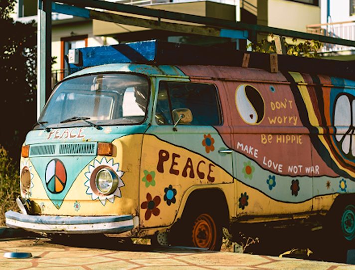 Colorful vintage van adorned with peace symbols and flowers, parked under a sunny sky.