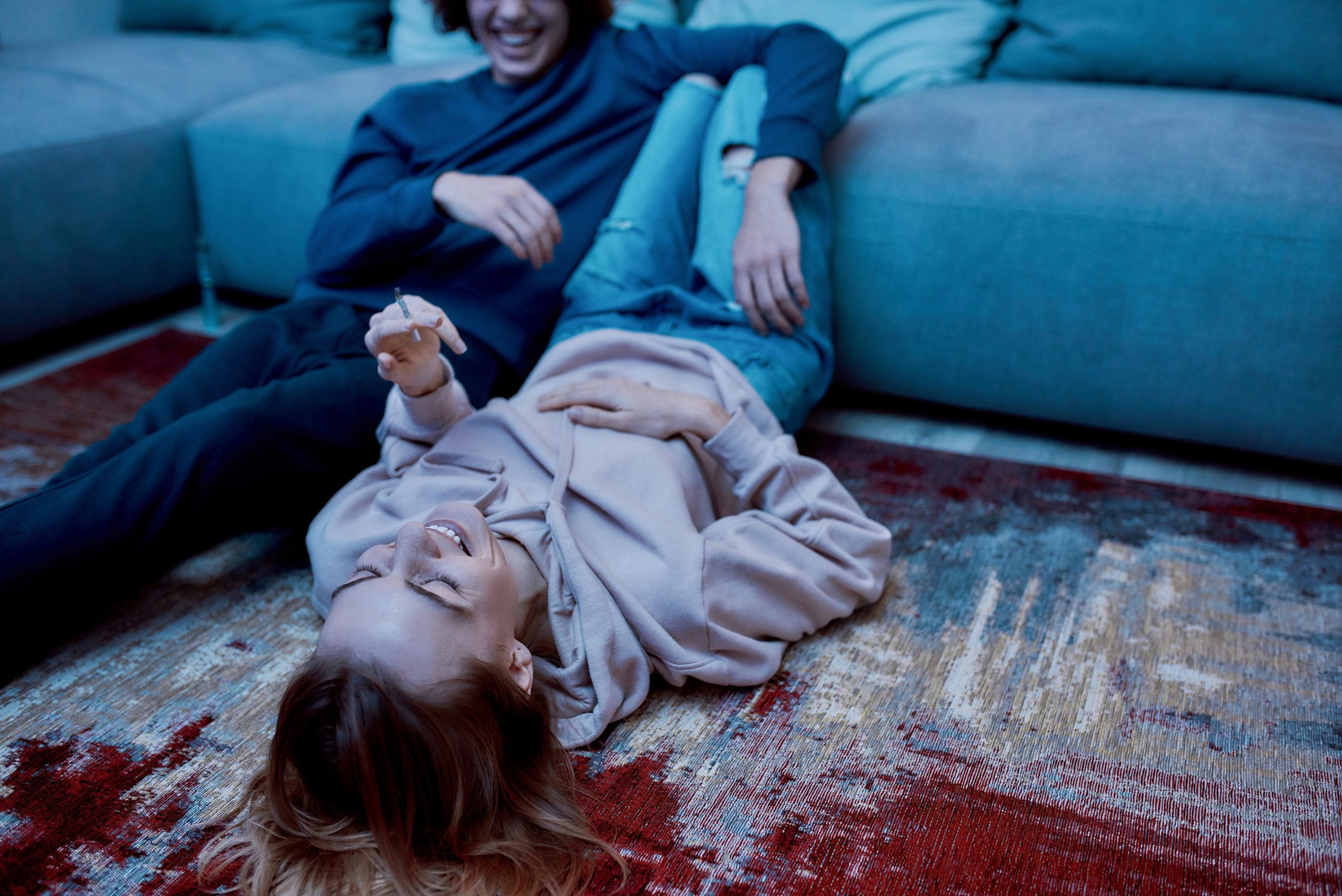 A couple laughs together on a colorful rug, with one lying down and the other playfully resting beside them.