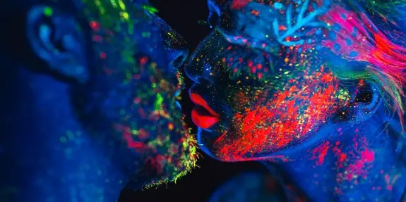 Couple with vibrant, glowing body paint sharing an intimate kiss against a dark background.