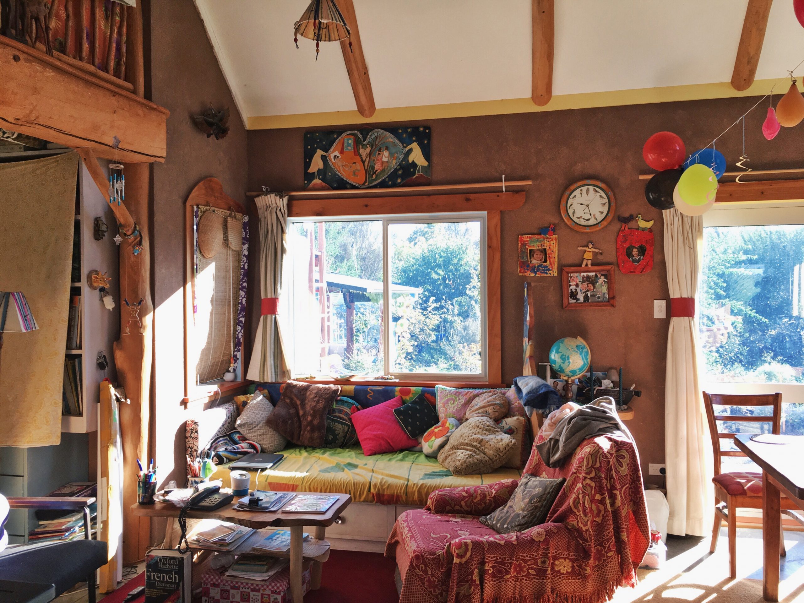 Cozy living space with colorful cushions, wooden beams, and sunlight streaming through a large window.