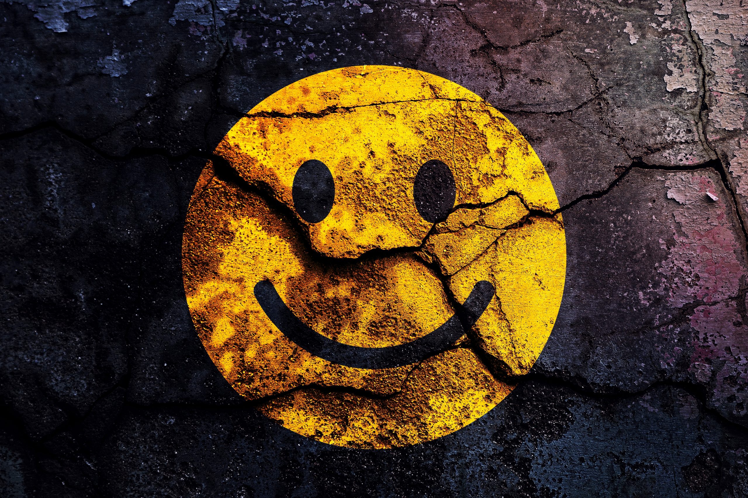 A cracked yellow smiley face on a textured, dark background, conveying a mix of joy and wear.