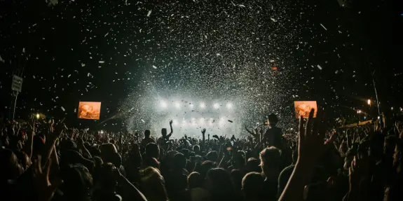 Crowd at a concert celebrating, with confetti falling and bright stage lights illuminating the scene.