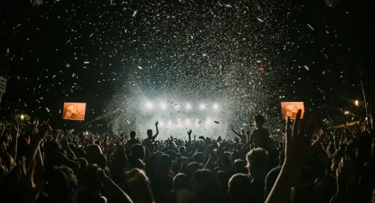 Crowd at a concert celebrating, with confetti falling and bright stage lights illuminating the scene.