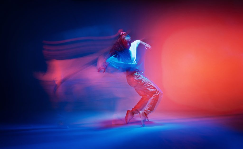 A dancer in motion, surrounded by vibrant blue and red lights, creating a dynamic, ethereal atmosphere.