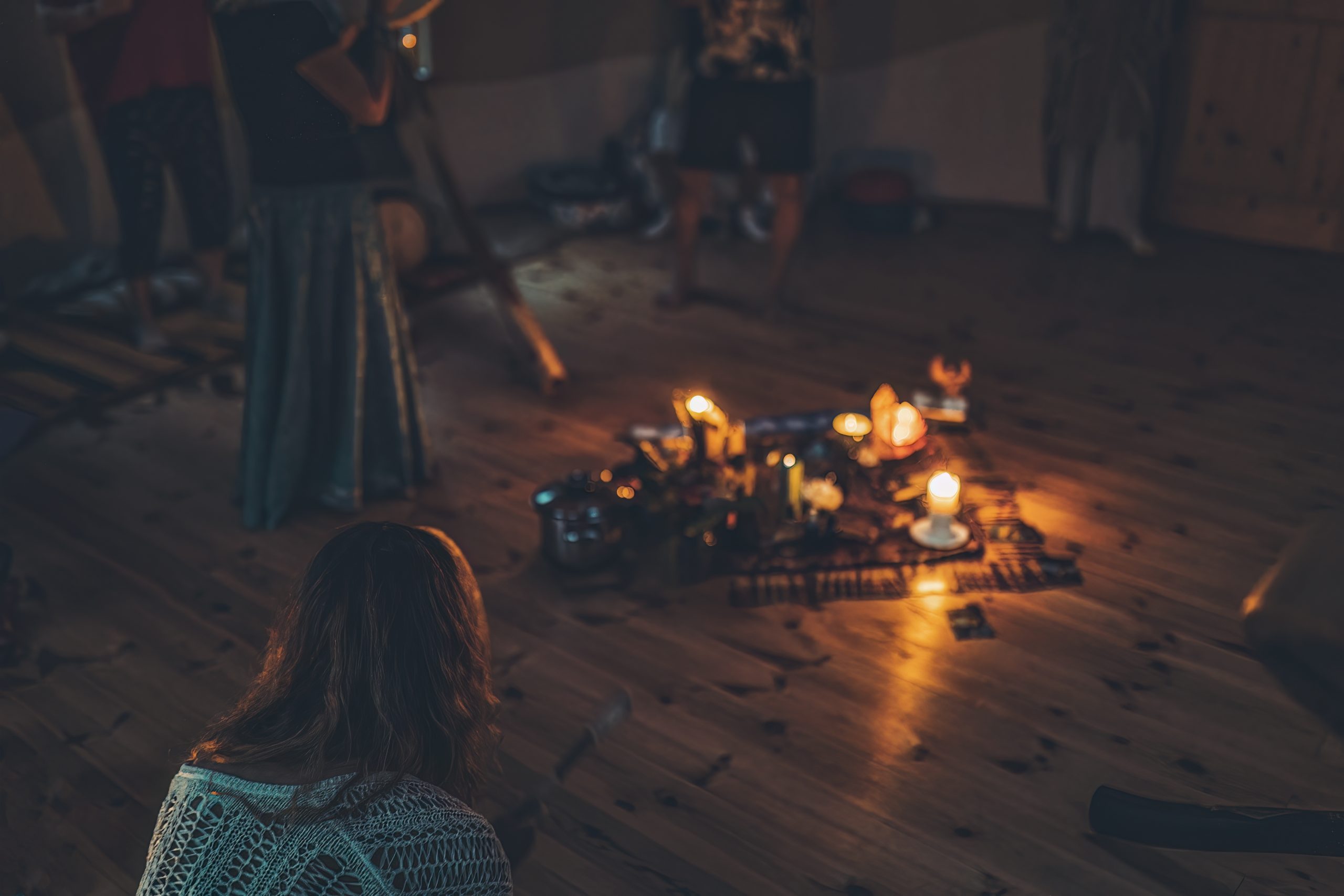 A dimly lit room with candles and offerings arranged on the floor, creating a serene and mystical atmosphere.