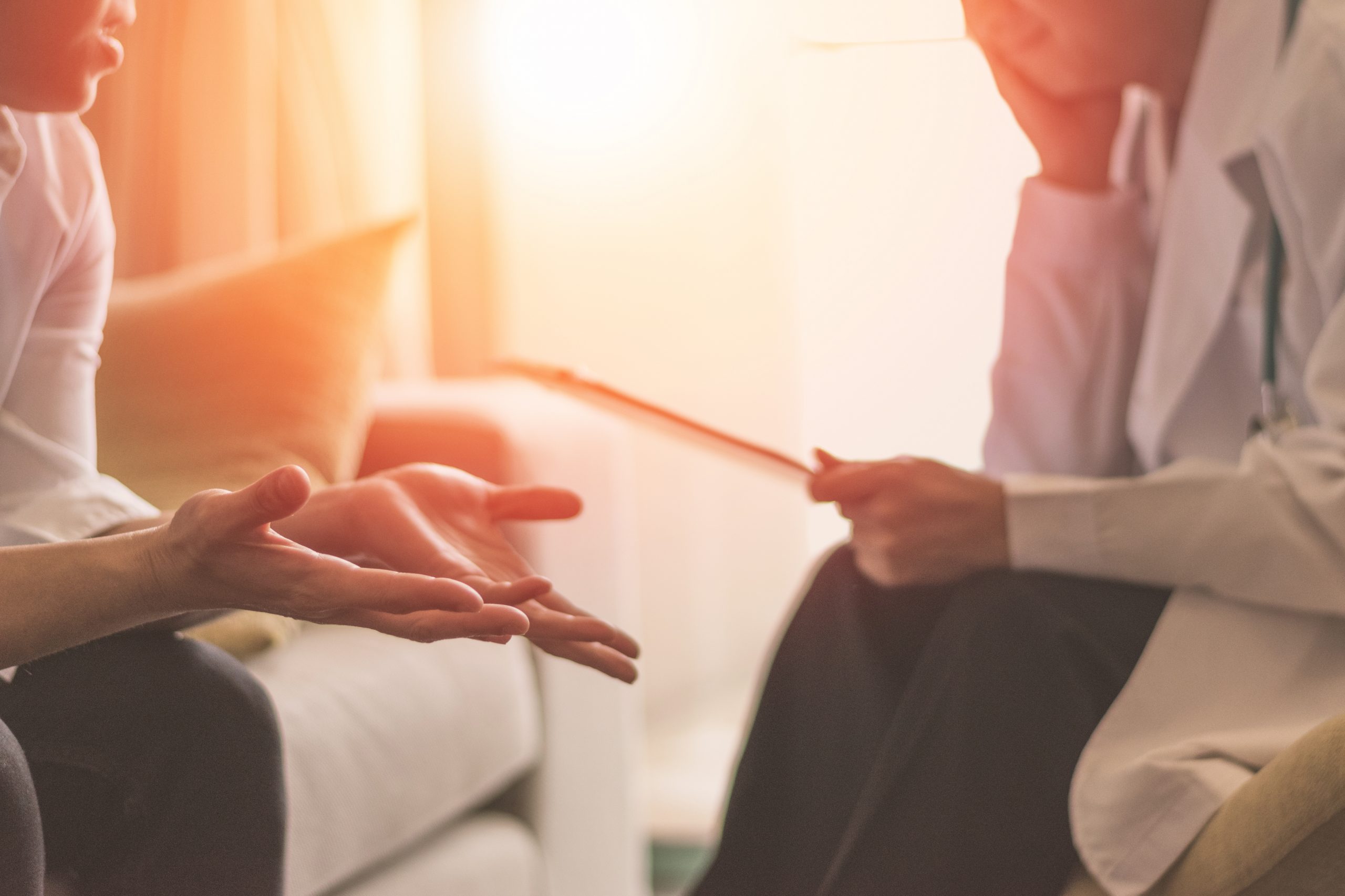 A doctor listens intently as a patient gestures, discussing concerns in a warmly lit room.