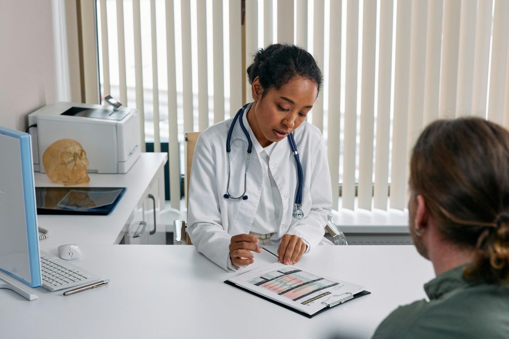 A doctor in a white coat discusses medical charts with a patient in a well-lit office.