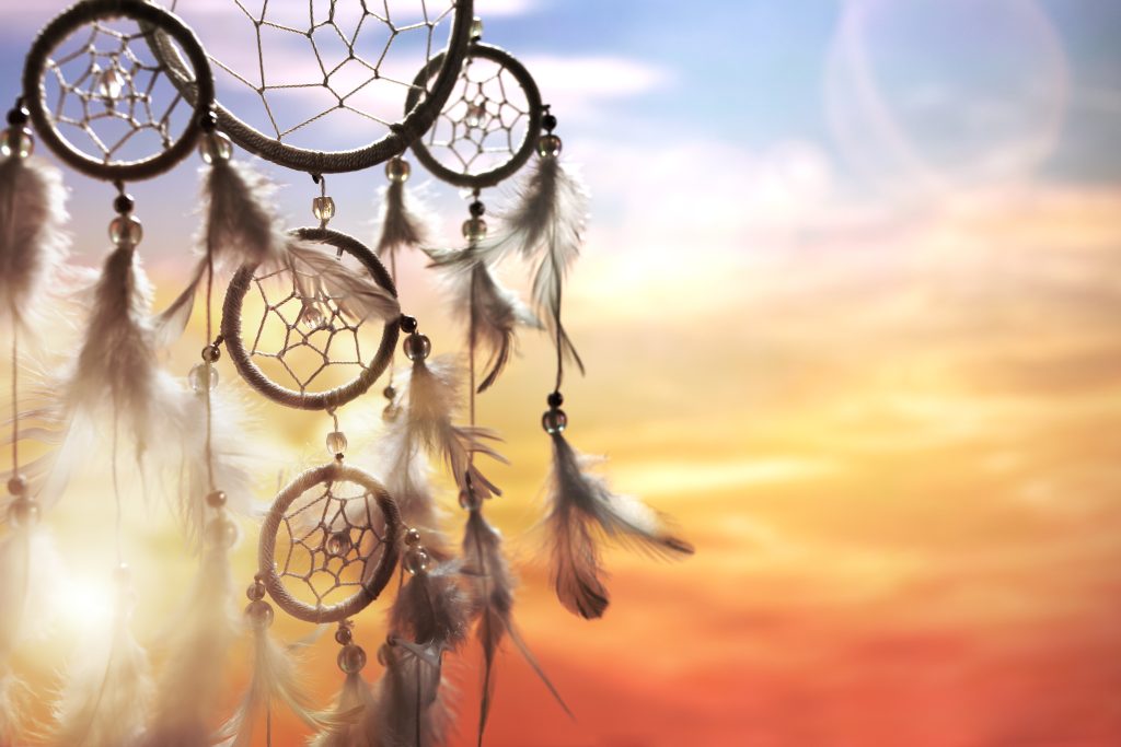 Dreamcatcher with delicate feathers and beads against a vibrant sunset sky, blending warm hues of orange and blue.