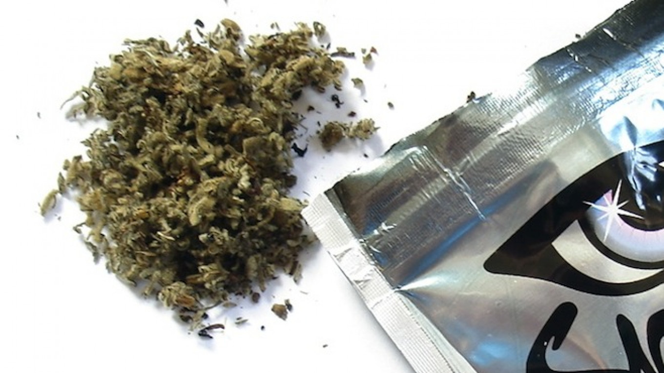 Dried herbal substance scattered beside a shiny, silver packaging with a graphic design.