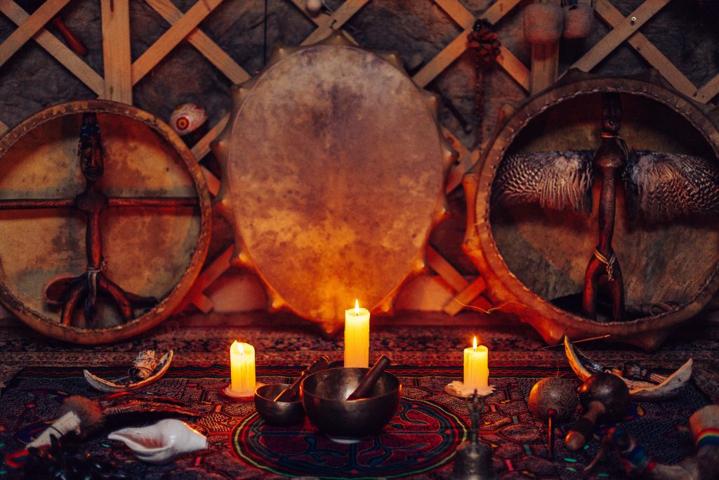Drums and a wooden figure surrounded by candles and ritual objects on a colorful patterned cloth.