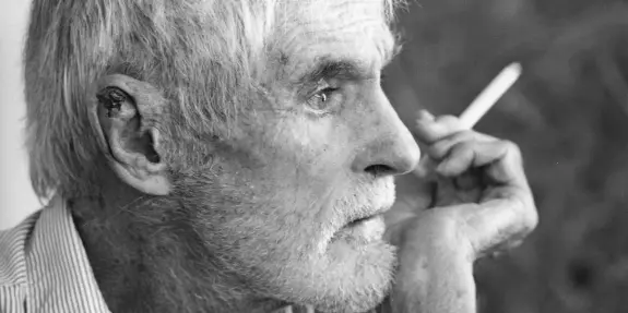 Elderly man with gray hair and a thoughtful expression, holding a cigarette and resting his chin on his hand.