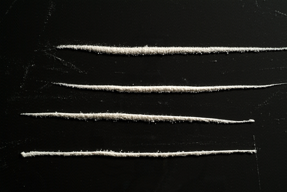 Four parallel lines of white powder on a dark surface, creating a stark contrast.
