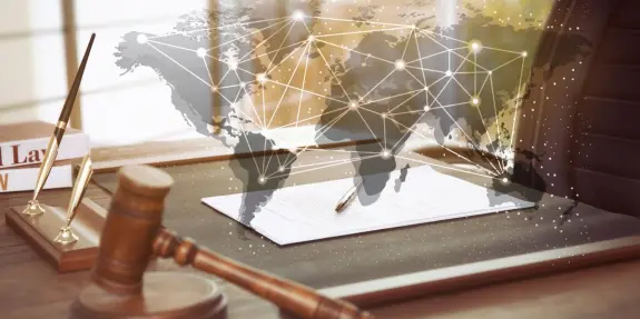 A gavel and legal documents on a desk, overlaid with a world map and network connections, symbolizing global law.