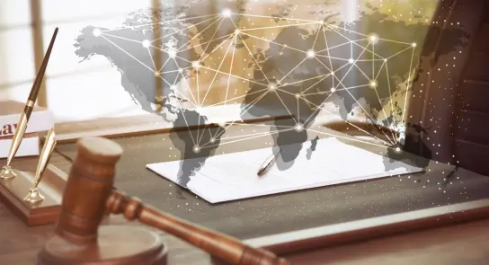 A gavel and legal documents on a desk, overlaid with a world map and network connections, symbolizing global law.