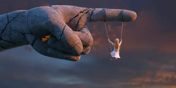 A giant stone hand points downwards, with a girl in a white dress swinging from its fingers against a dramatic sunset sky.