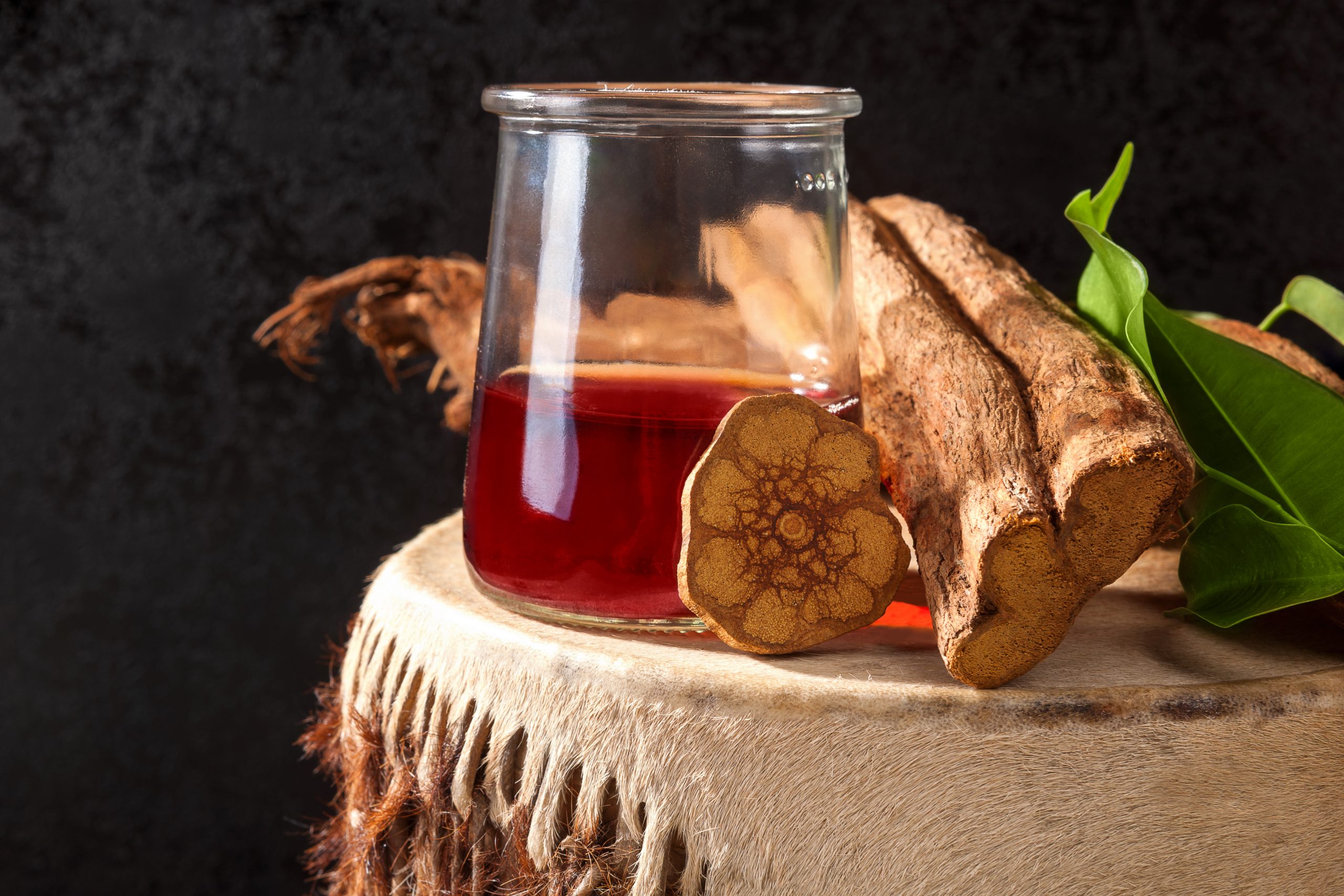 Glass jar filled with dark liquid, surrounded by roots and green leaves on a textured surface.