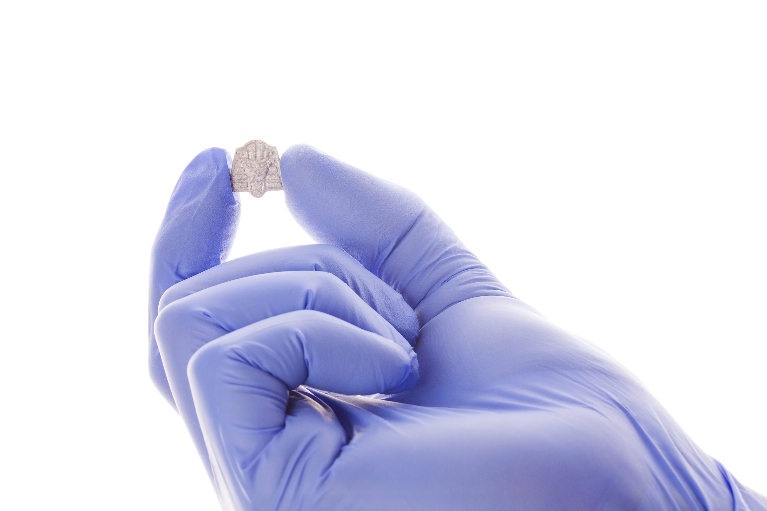 A gloved hand holds a small, silver object shaped like a hand against a white background.