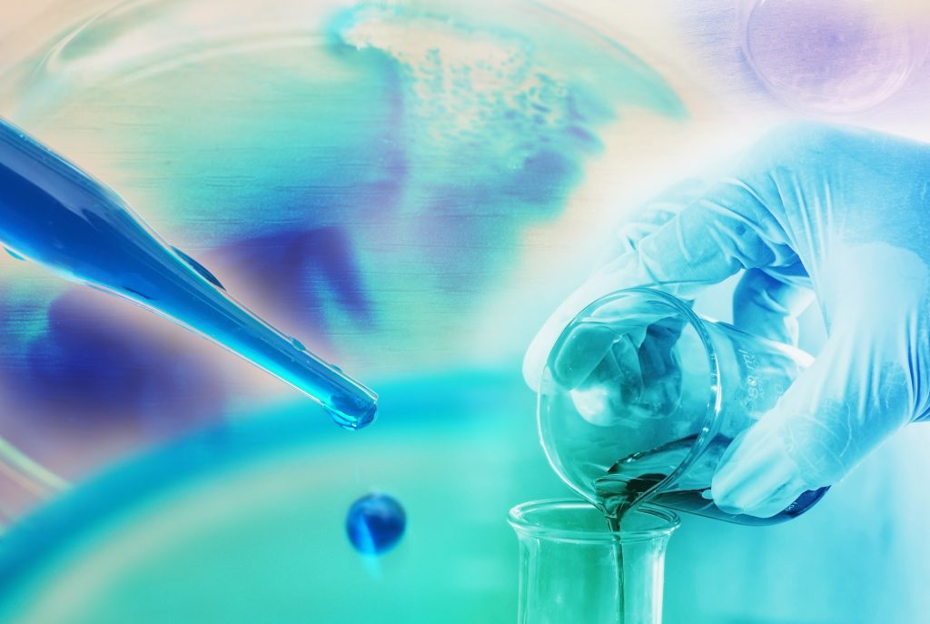 A gloved hand pours liquid from a beaker into a test tube, with a pipette and colorful laboratory background.
