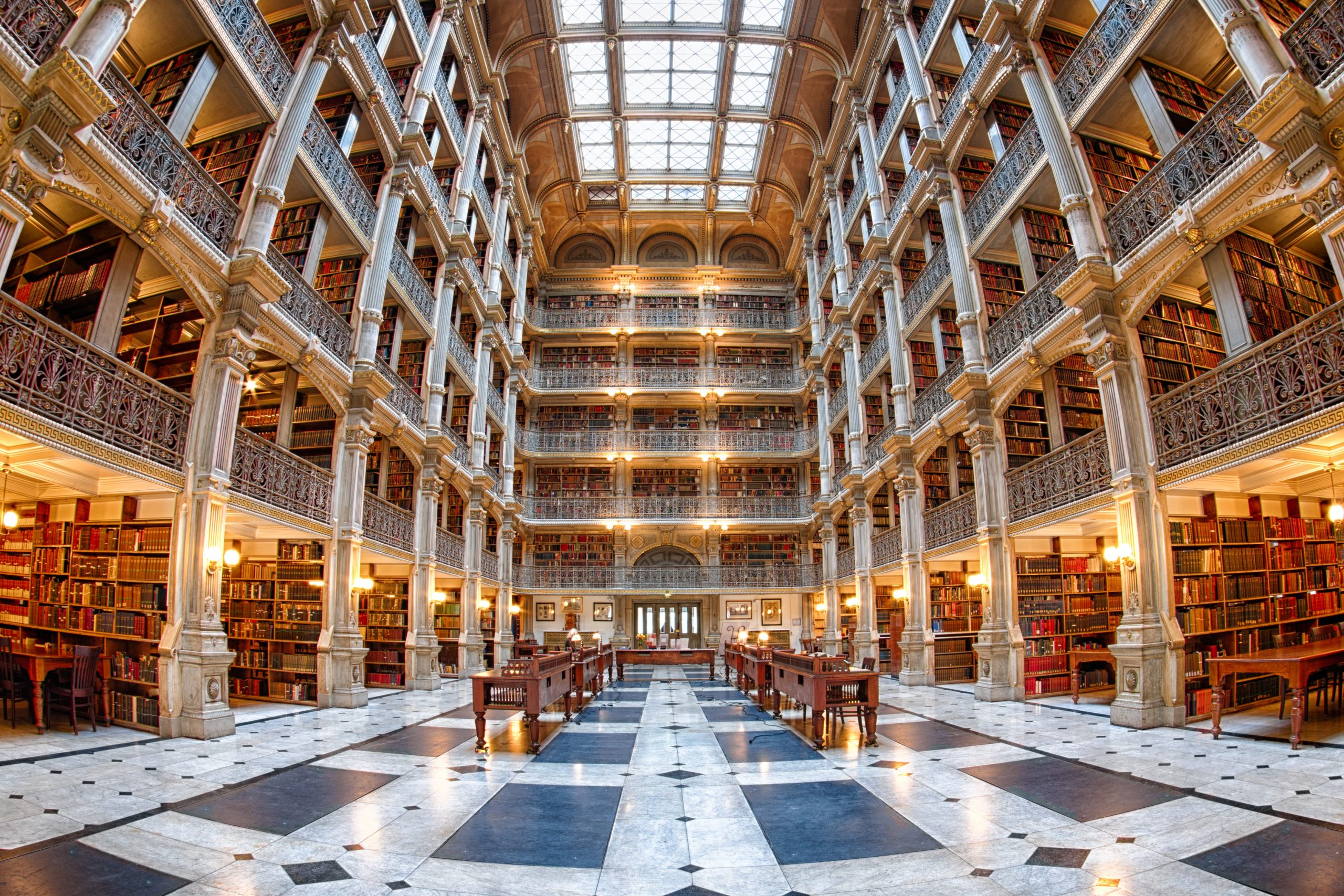 Grand library interior with towering bookshelves, intricate railings, and a glass ceiling, illuminated by warm lights.