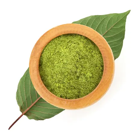 Green powder in a wooden bowl, placed on a large green leaf.