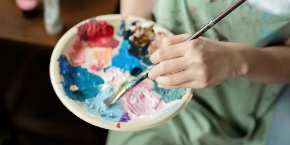 A hand holding a paintbrush above a palette filled with vibrant colors, ready for artistic creation.